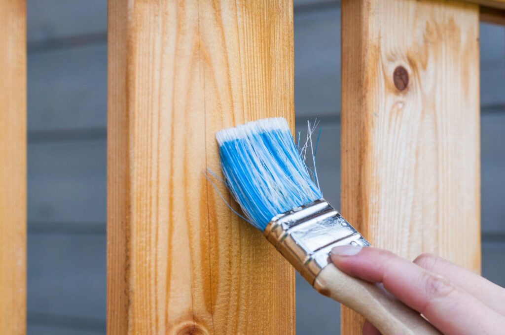 pexels-photo-221027-221027 A hand painting a wooden fence plank with a blue paintbrush outdoors. Perfect for DIY and renovation themes.